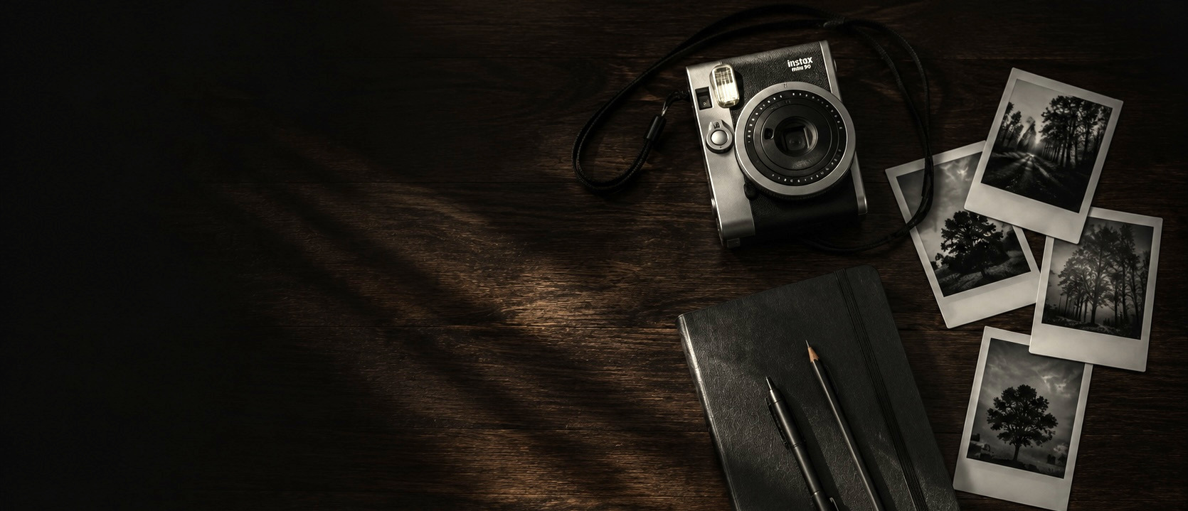 Instax camera, instant photos, notebook and pens on a dark wooden desk